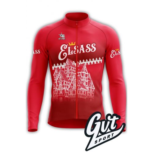 L'image présente un maillot de cyclisme à manches longues de couleur rouge vif. 
Sur le devant, une illustration blanche et détaillée montre des maisons à colombages traditionnelles alsaciennes, avec leurs structures en bois et leurs toits distinctifs. A
