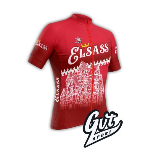 La photo représente le maillot cycliste Gvt Sport Elsass Cyclo de couleur rouge vue de face. 
Sur le devant, une illustration blanche et détaillée montre des maisons à colombages traditionnelles alsaciennes, avec leurs structures en bois et leurs toits d